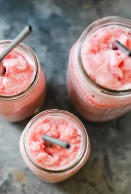 Frosted Strawberry Lemonade in a glass with strawberries and lemon slices