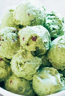 A bowl of mint chocolate chip ice cream topped with chocolate chips and fresh mint leaves.