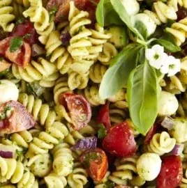 Pasta salad with pesto, vegetables, and fresh basil in a bowl