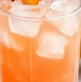 Chilled glass of peach lemonade garnished with fresh peach slices and mint leaves.