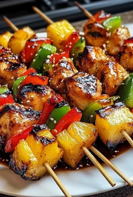 Grilled pineapple chicken kabobs garnished with herbs on a platter.