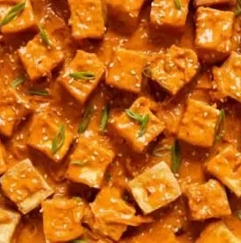 Spicy tofu dish topped with creamy coconut sauce and fresh herbs