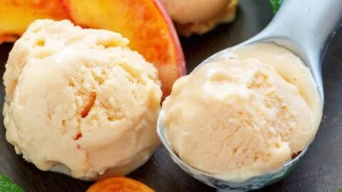 Creamy high protein peach ice cream in a bowl with fresh peach slices