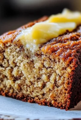 Slice of moist banana bread on a wooden board with bananas in the background.