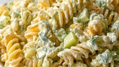 A bowl of simple dill pickle pasta salad with fresh ingredients and herbs.