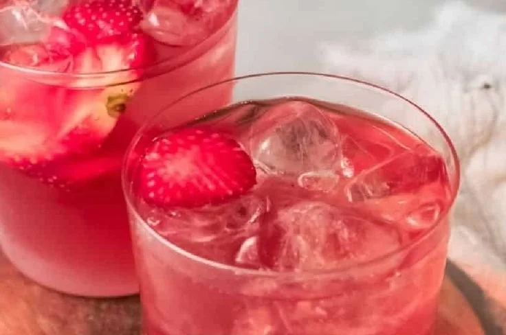 A refreshing glass of strawberry iced tea garnished with fresh strawberries and mint.