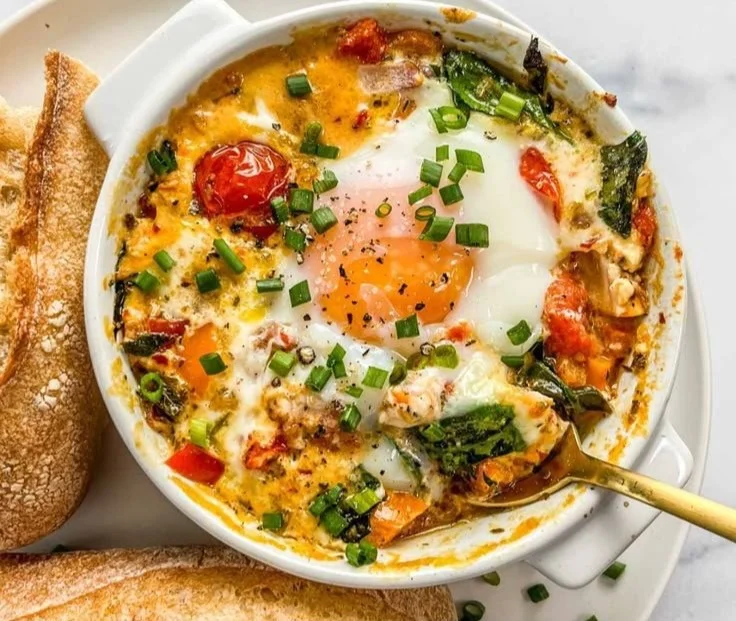 Baked feta eggs with tomatoes and spinach served in a dish