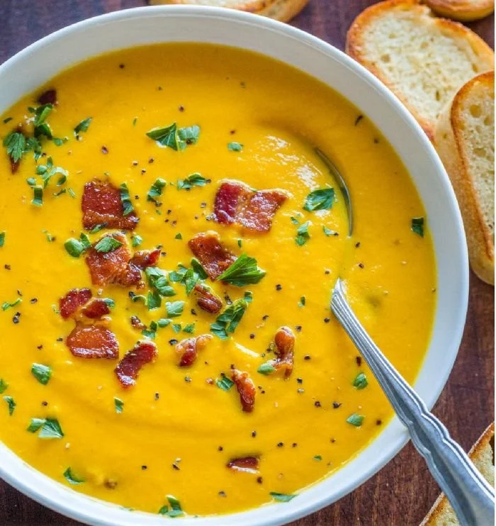 Bowl of creamy carrot soup garnished with herbs and served with bread