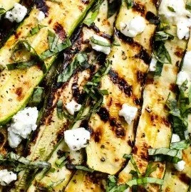 Grilled zucchini topped with goat cheese, basil, and honey on a plate