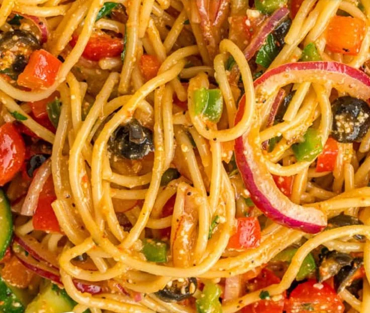 Colorful bowl of spaghetti salad with vegetables and dressing